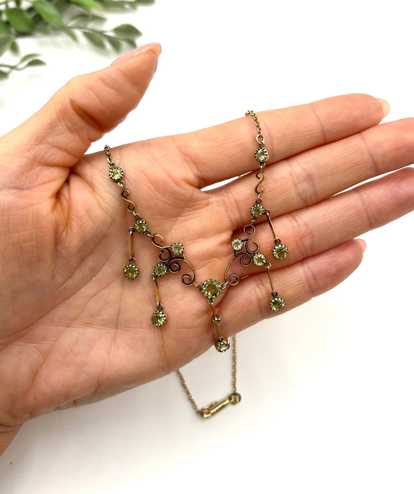 A yellow gold swag necklace with peridot drops, held in a hand