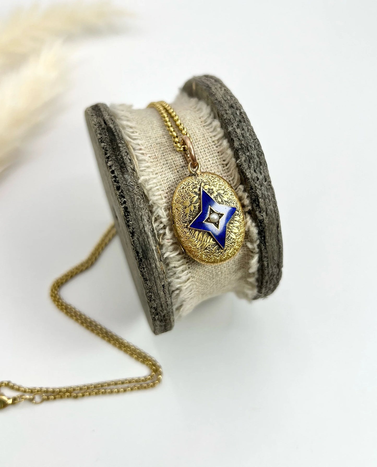 An oval yellow gold locket with a blue enamel star and seed pearl centre, with a chain