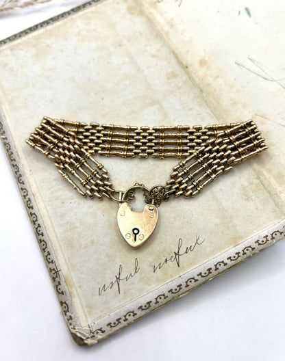 A yellow gold gate bracelet with heart shaped padlock clasp, on an antique book