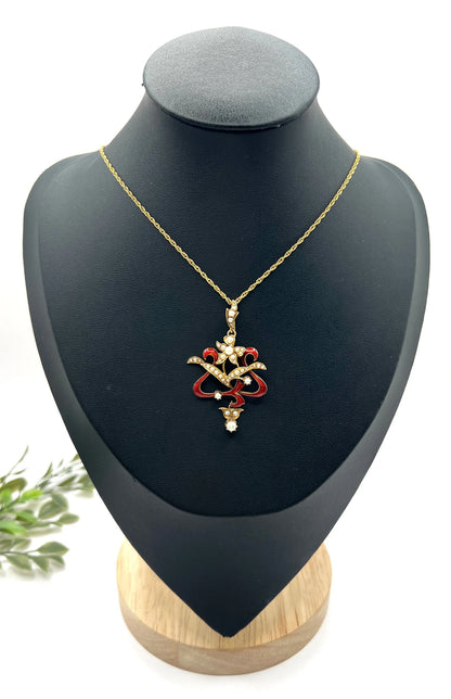 A floral pendant in yellow gold with seed pearls and red enamel, with a chain, on a black jewellery bust