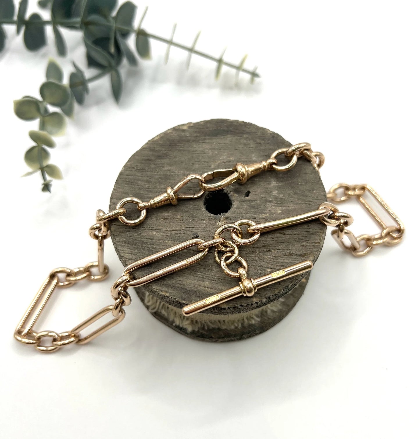A rose gold trombone and fetter link Albert chain lying on top of a wooden object, on a white background