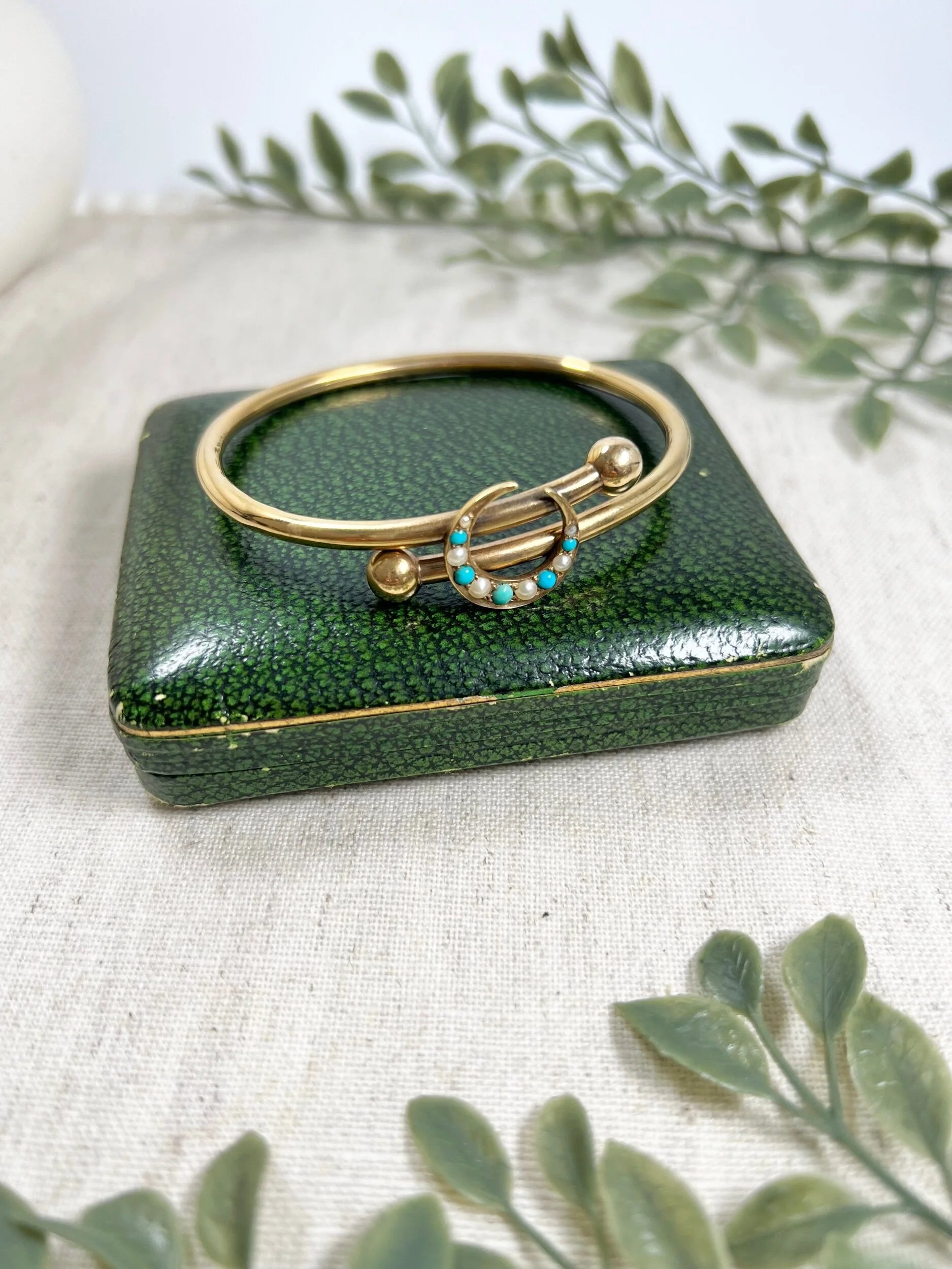 A yellow gold crossover bangle bracelet with a pearl and turquoise crescent moon centre