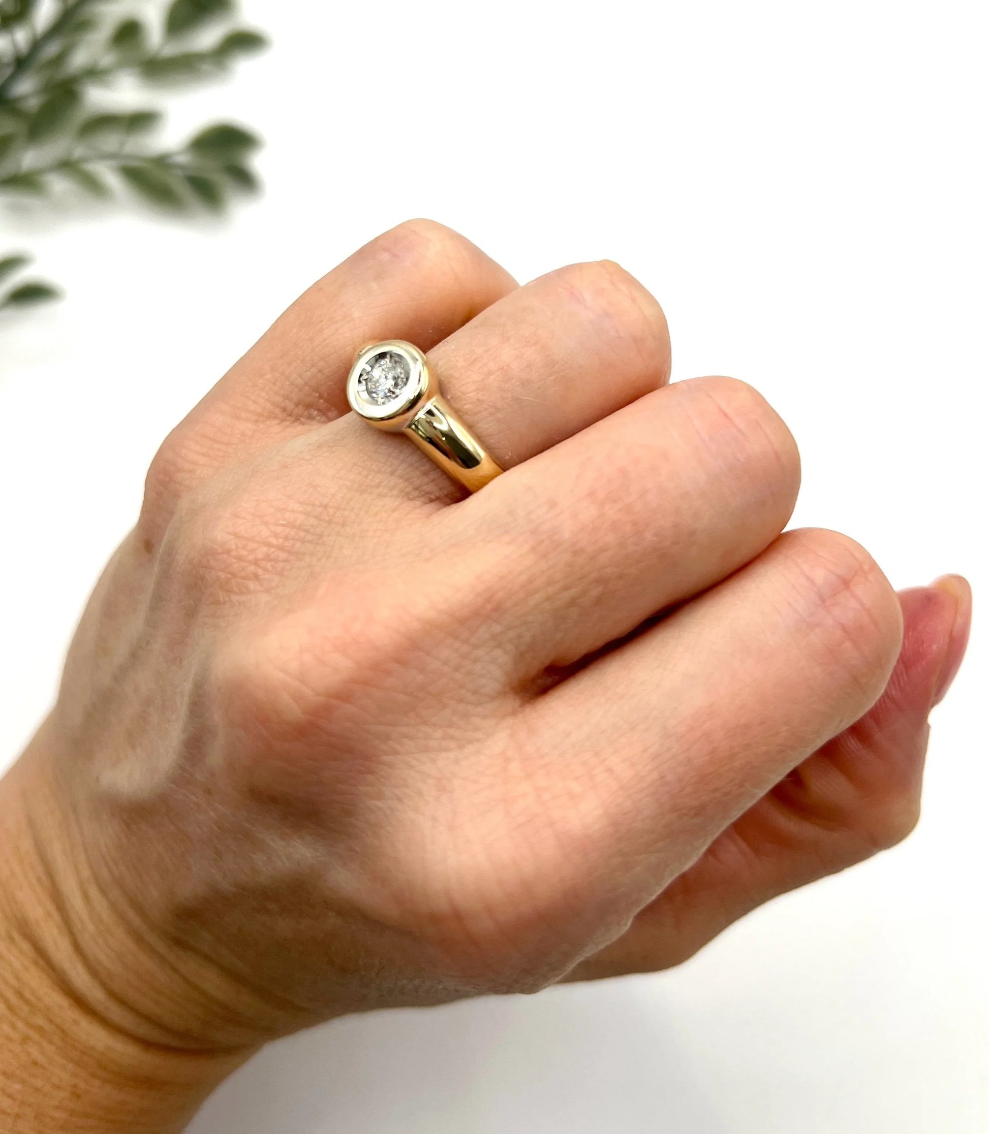 A single stone brilliant cut diamond ring bezel set in yellow gold, modelled on a hand