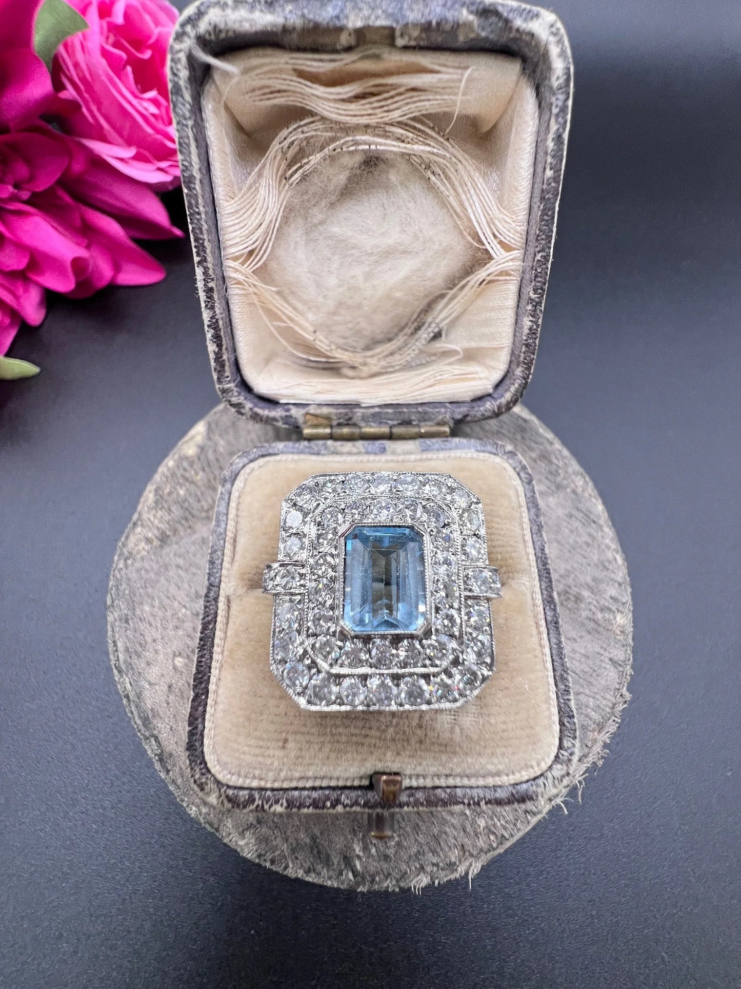 An octagonal shaped cluster ring with an aquamarine centre surrounded by two rows of diamonds, in platinum, in a ring box