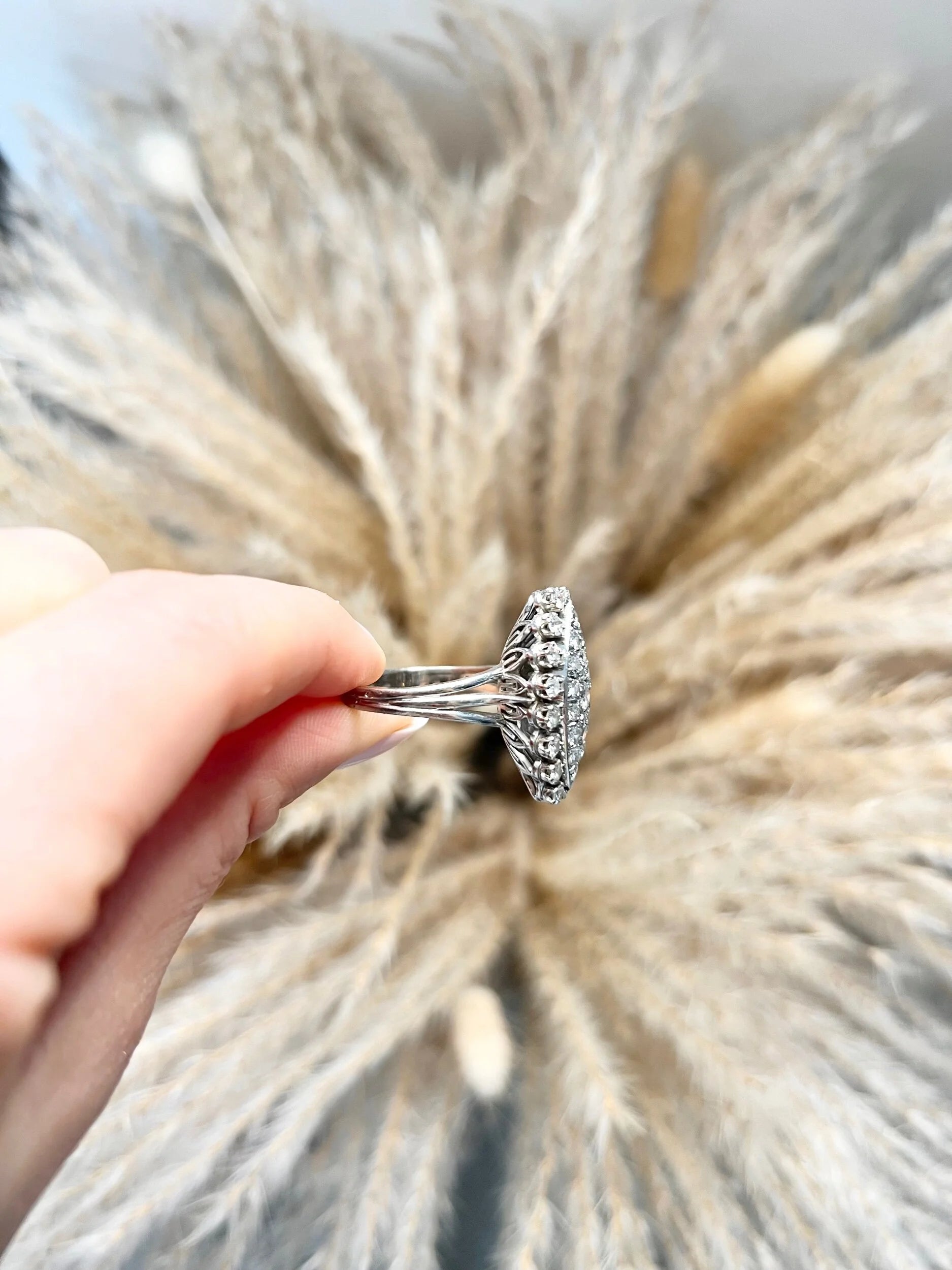 A navette shaped diamond cluster ring in white metal, held in a hand