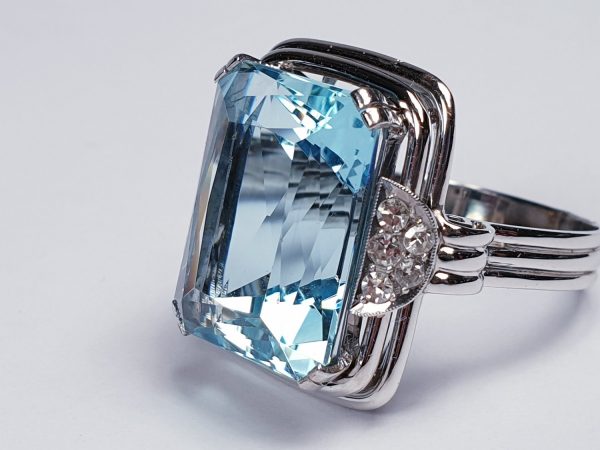 Art Deco Aquamarine and Diamond Dress Ring; a striking 14.80 carat emerald-cut aquamarine accented with half moon diamond cluster shoulders, on a three wire platinum band. Circa 1930s