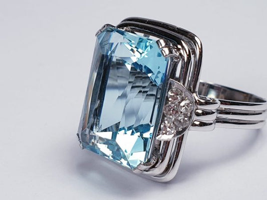 Art Deco Aquamarine and Diamond Dress Ring; a striking 14.80 carat emerald-cut aquamarine accented with half moon diamond cluster shoulders, on a three wire platinum band. Circa 1930s