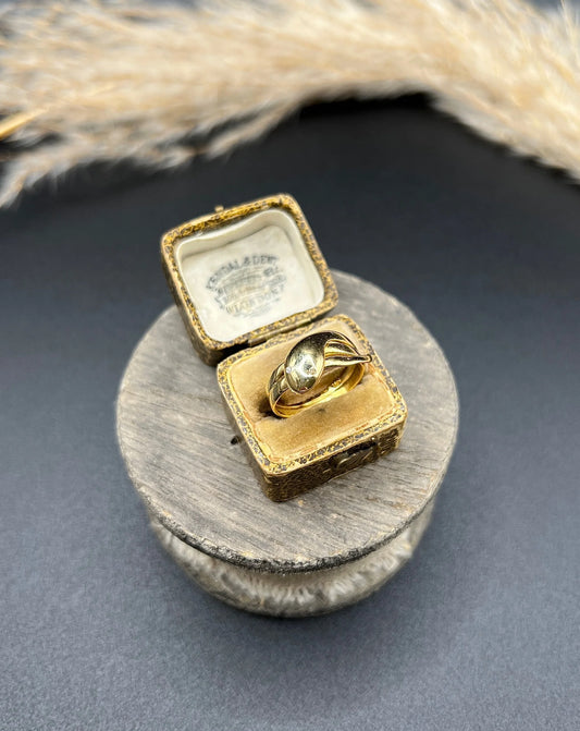 A yellow gold coiled snake ring with diamond eyes, in a box