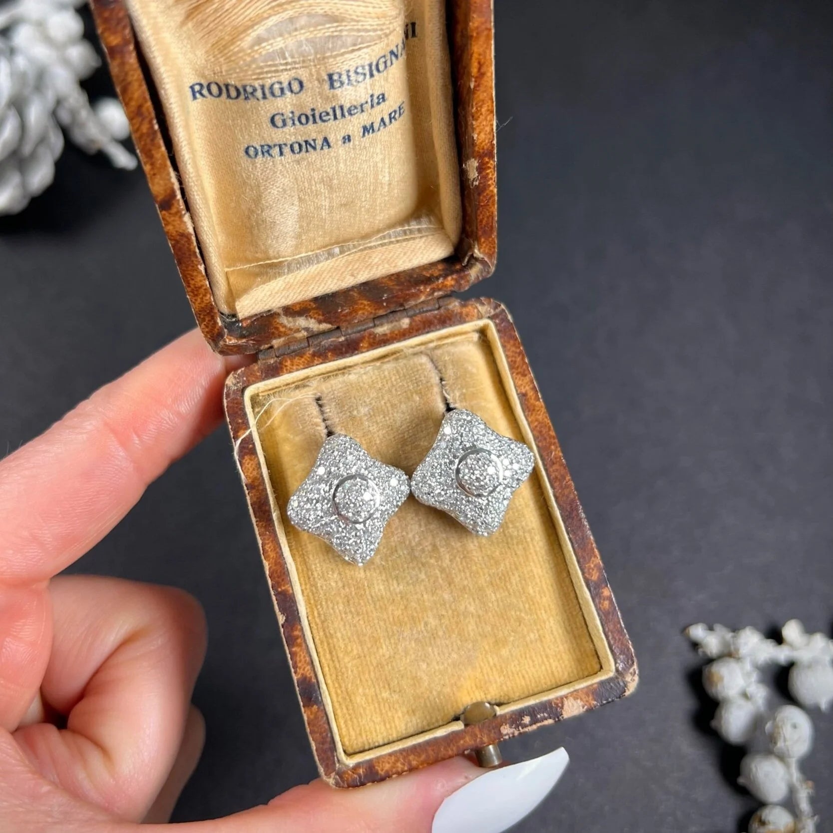A pair of diamond cluster stud earrings in white gold, in an antique box, held in a hand