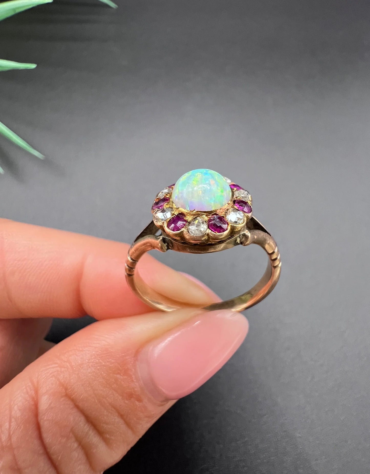 A daisy style cluster ring in rose gold with opal, ruby and diamond, held in a hand