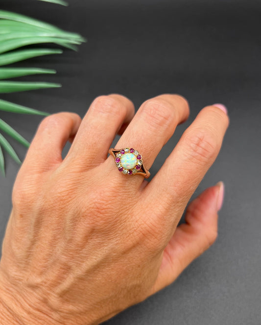 A daisy style cluster ring in rose gold with opal, ruby and diamond, modelled on a hand