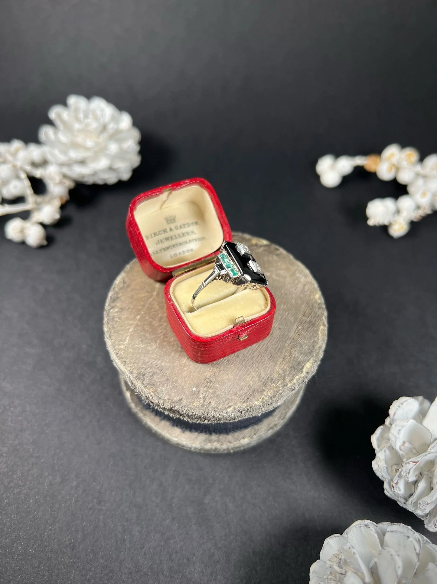 A geometric black onyx ring with diamonds and emeralds in white gold, in an antique ring box