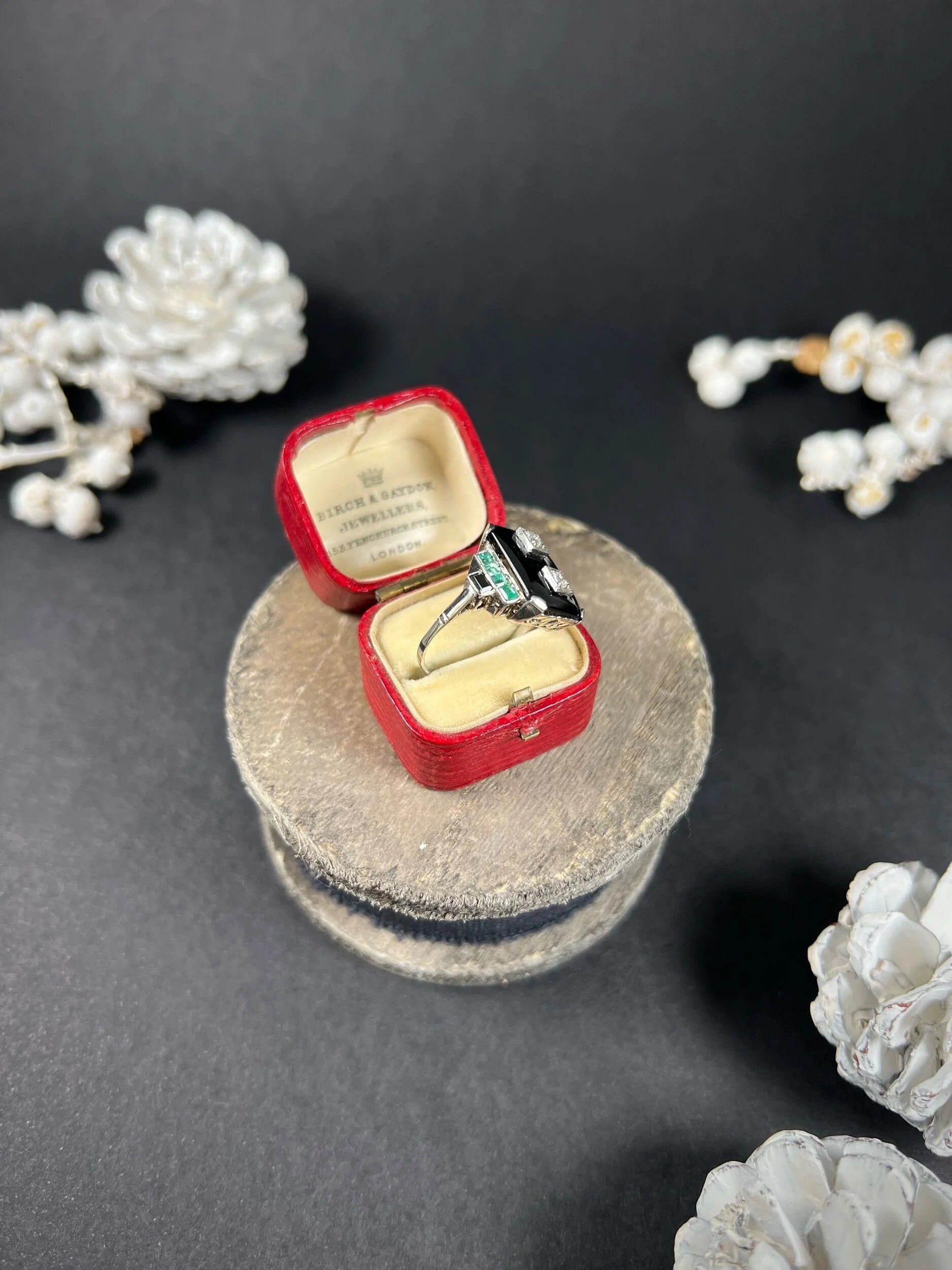 A geometric black onyx ring with diamonds and emeralds in white gold, in an antique ring box