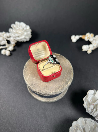 A geometric black onyx ring with diamonds and emeralds in white gold, in an antique ring box