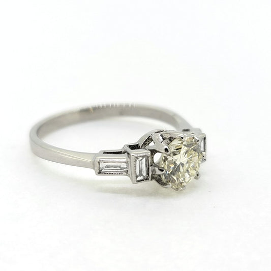 A brilliant cut and baguette cut diamond engagement ring in white metal, against a white background