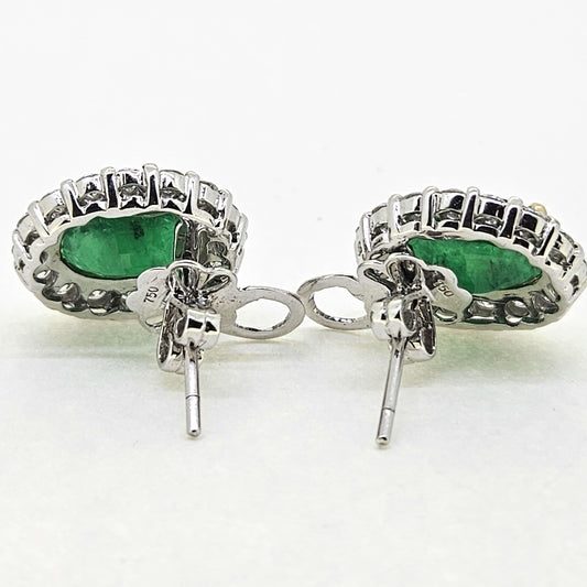 A pair of emerald and diamond oval cluster earrings in white gold, viewed from behind, on a white background