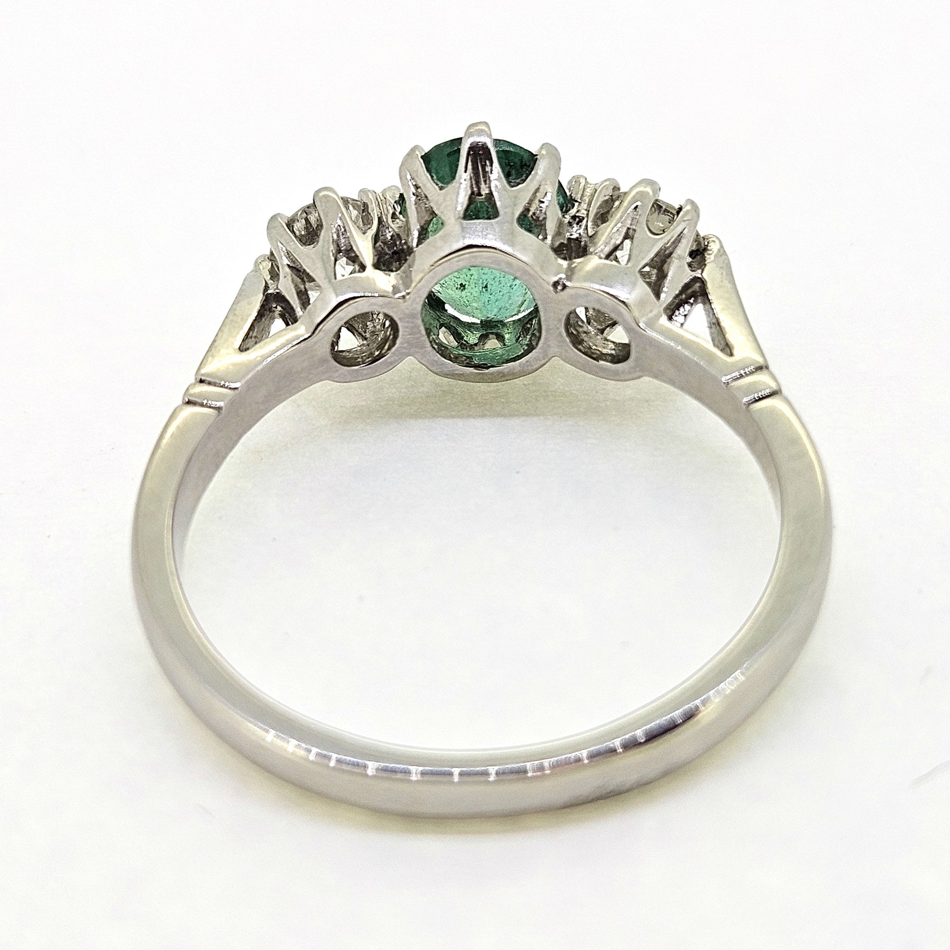 A platinum emerald and diamond three stone ring, viewed from behind, on a white background