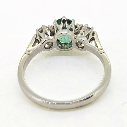A platinum emerald and diamond three stone ring, viewed from behind, on a white background