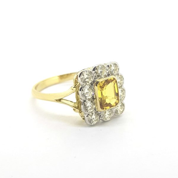 Vintage Yellow Sapphire and Diamond Cluster Ring; 1.20ct step-cut yellow sapphire surrounded by ten round brilliant-cut diamonds totalling 1 carat, in 18ct yellow gold with split shoulders. Circa 1970