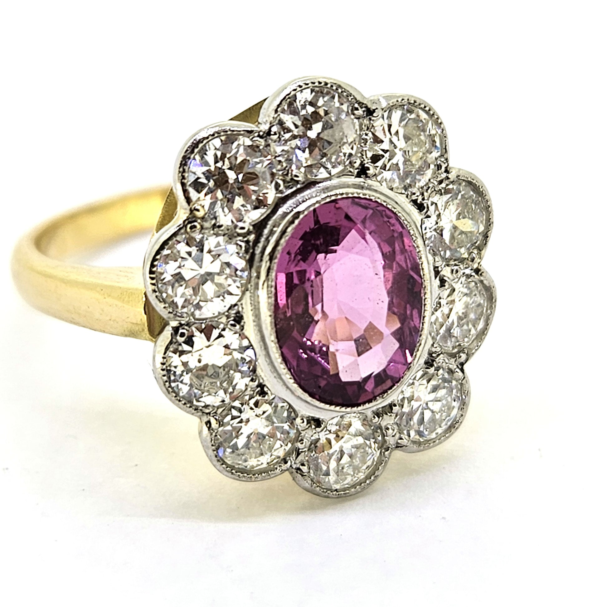 A pink sapphire and round diamond oval shaped cluster ring in yellow and white metal, on a white background