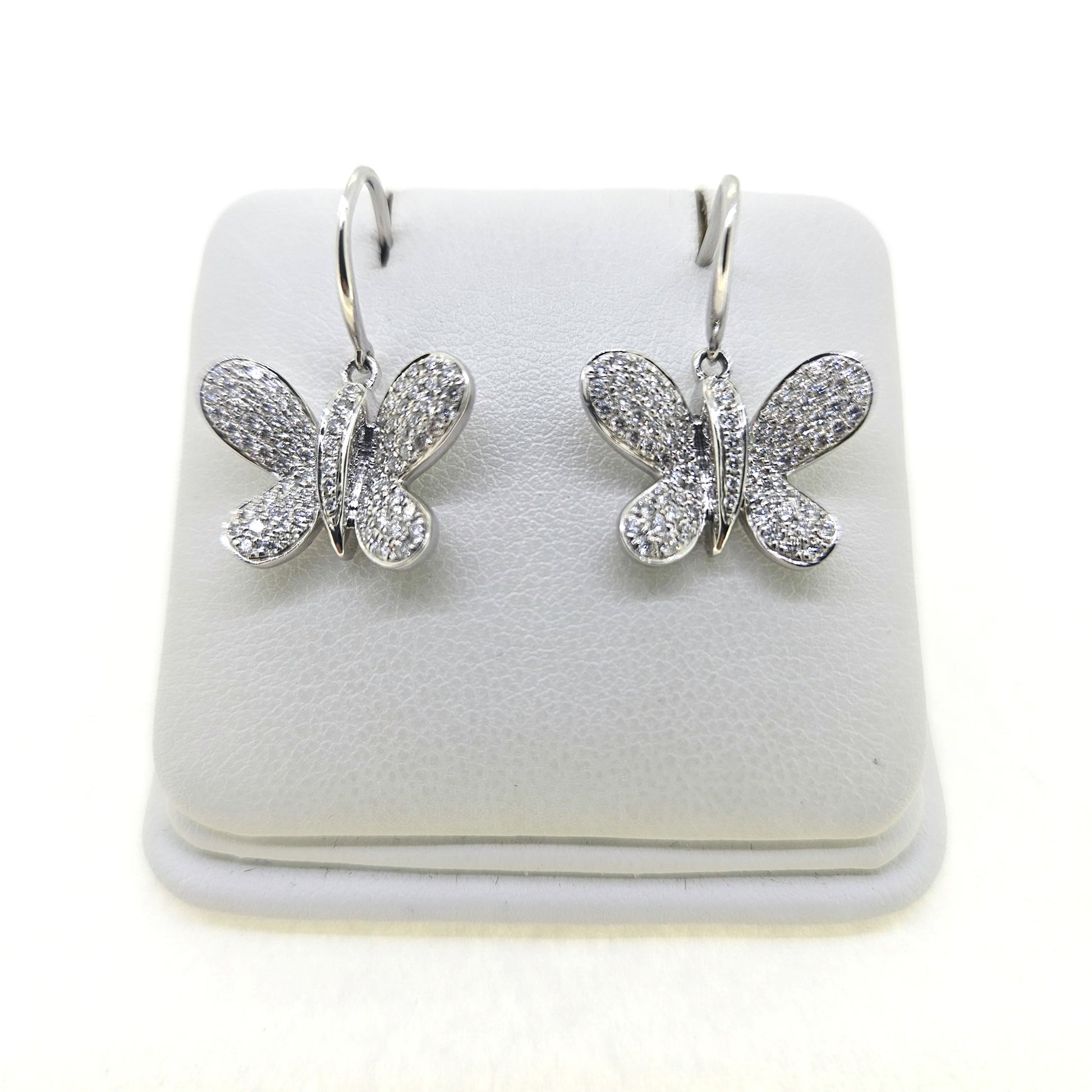 A pair of butterfly shaped diamond set earrings with hook fittings in white gold, on a white background