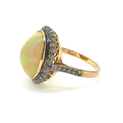 A cabochon opal and diamond oval cluster ring in gold and silver, viewed from the side, on a white background