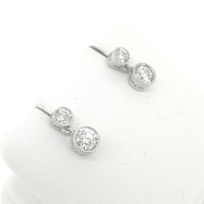 A pair of round brilliant cut diamond double drop earrings in white metal, on an earring display pad, on a white background