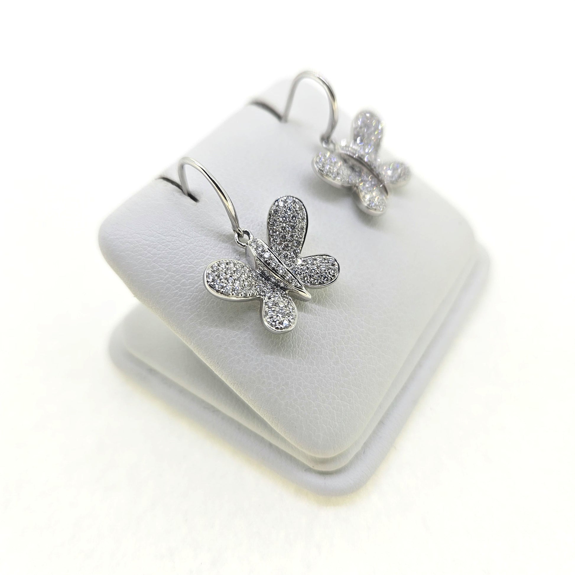 A pair of butterfly shaped diamond set earrings with hook fittings in white gold, on a white background