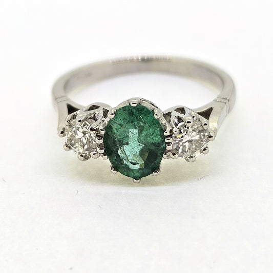 A platinum emerald and diamond three stone ring, on a white background