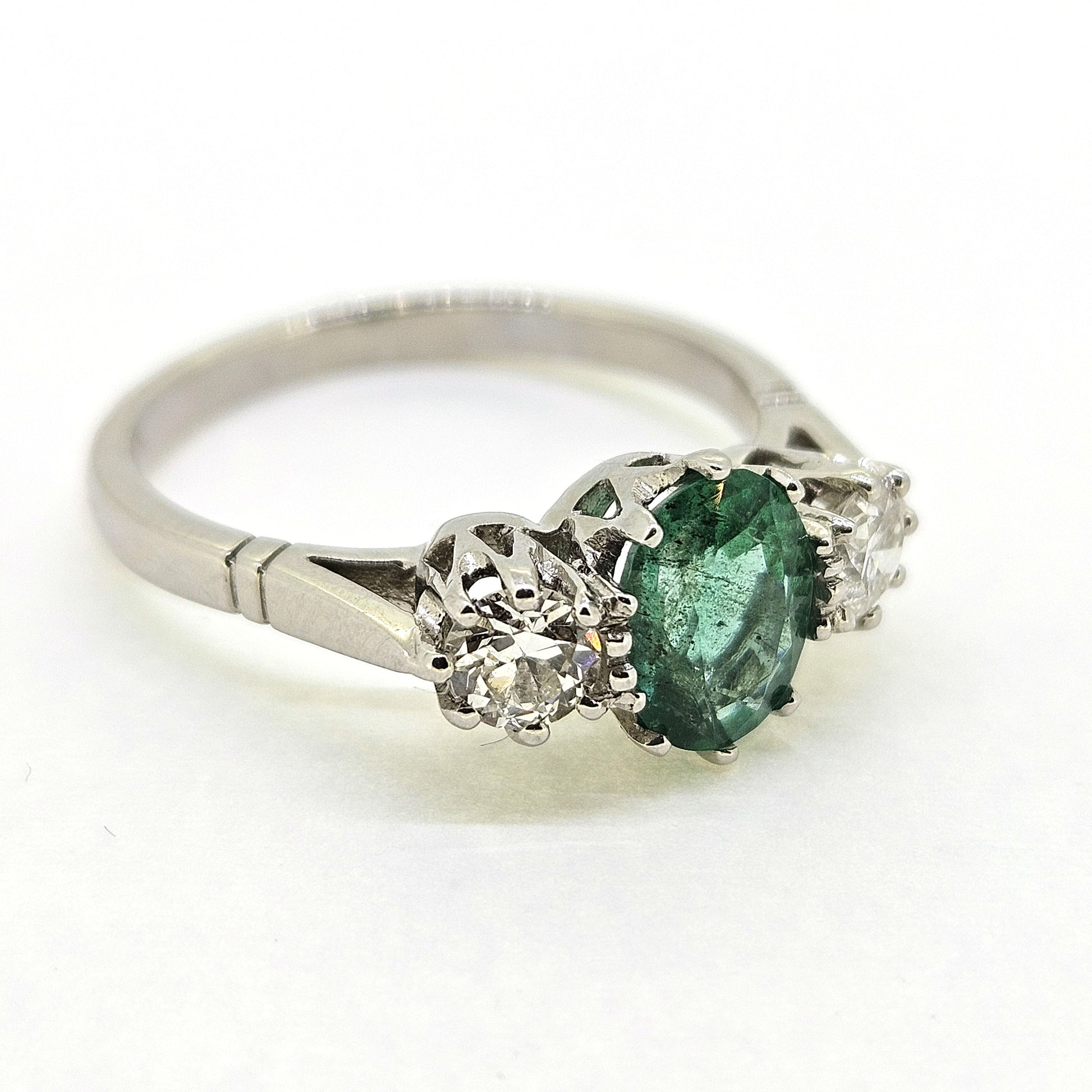 A platinum emerald and diamond three stone ring, on a white background