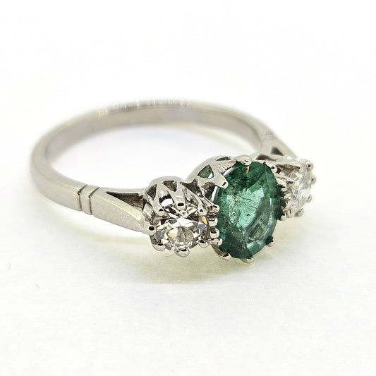 A platinum emerald and diamond three stone ring, on a white background