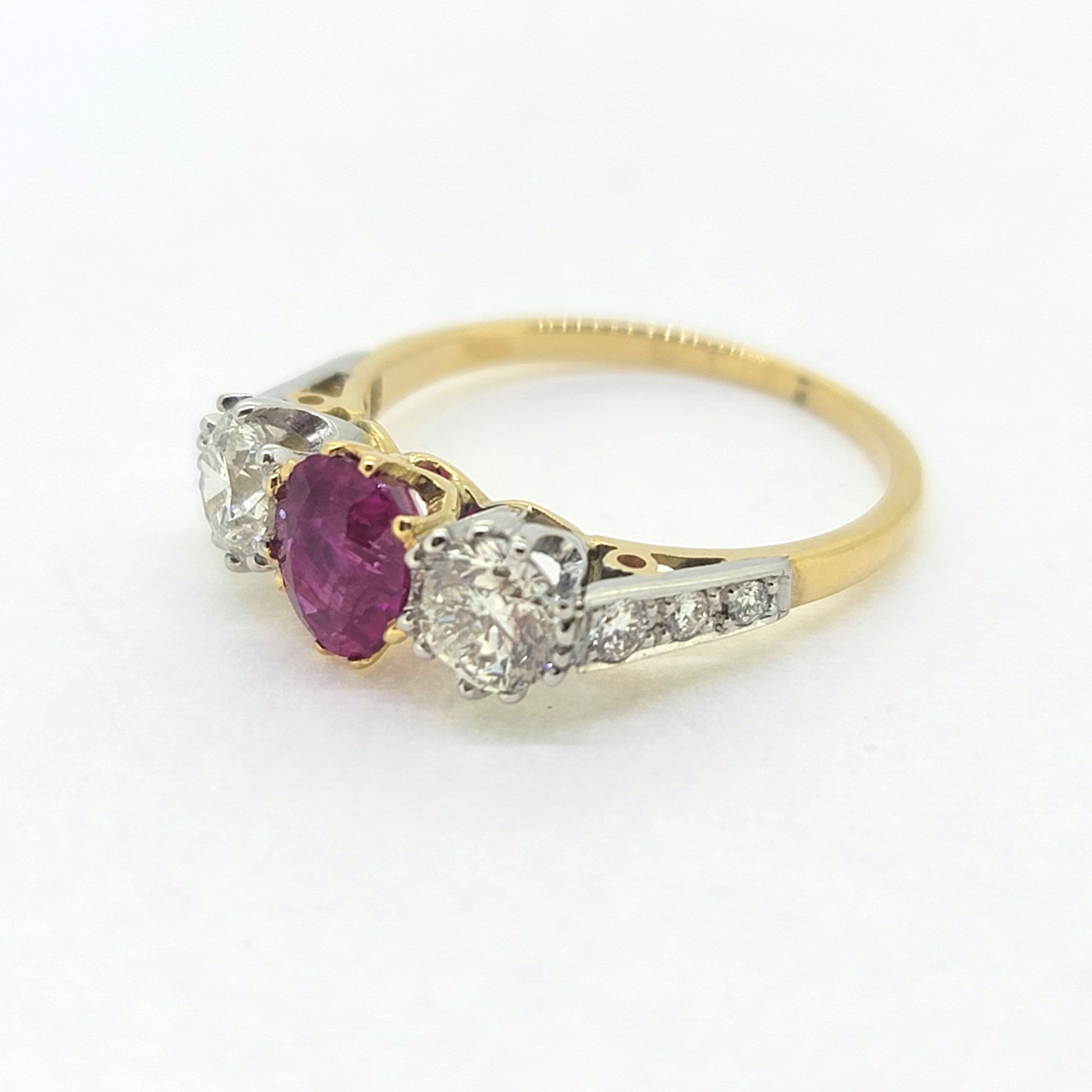 A three stone ruby and diamond ring in yellow and white gold, against a white background