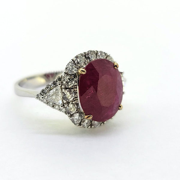 Contemporary 4.79ct Ruby and Diamond Cluster Engagement Ring, 4.79ct oval red ruby flanked by trillion diamonds all within a brilliant-cut diamond halo border in 18ct white gold