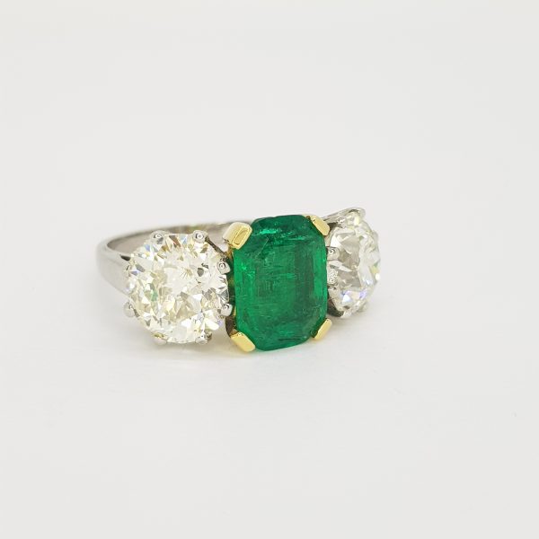 Colombian Emerald and Diamond Three Stone Ring; central certified 2.45ct emerald-cut Colombian emerald flanked by 4.56cts diamonds, in 18ct white gold