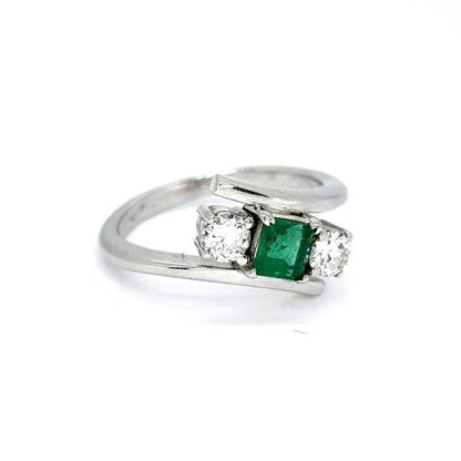 Emerald and Diamond Crossover Three Stone Ring; central princess-cut emerald flanked by brilliant-cut diamonds, in 18ct white gold with stylish crossover design