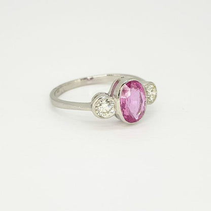 Pink Sapphire and Diamond Three Stone Ring in Platinum; central collet set 1.35ct oval pink sapphire flanked by 0.40cts brilliant cut diamonds