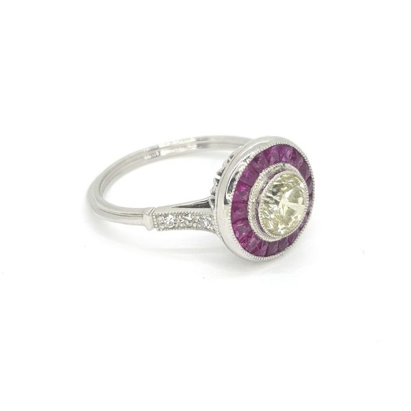 Art Deco Style Yellow Diamond and Calibre Ruby Target Cluster Ring; central 1ct yellow diamond surrounded by a halo of calibre-cut rubies, with diamond set shoulders, in 18ct white gold