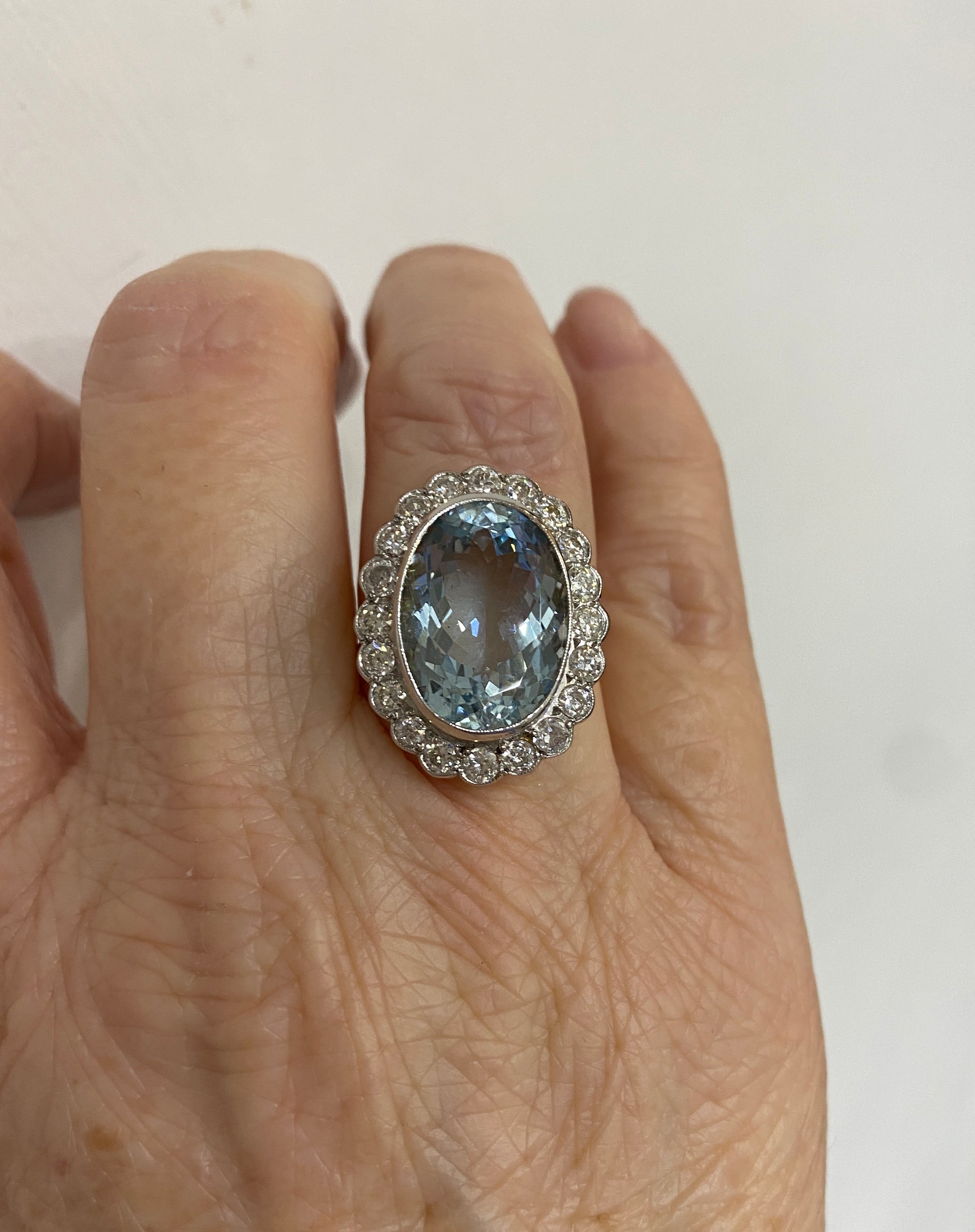 An aquamarine and diamond oval shaped cluster ring in yellow and white gold, modelled on a ring finger