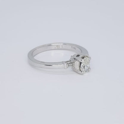 Diamond Solitaire Engagement Ring with Baguette Shoulders in 18ct White Gold; featuring a central claw-set round brilliant-cut diamond flanked by tapered baguette cut diamonds to the shoulders in rubover settings