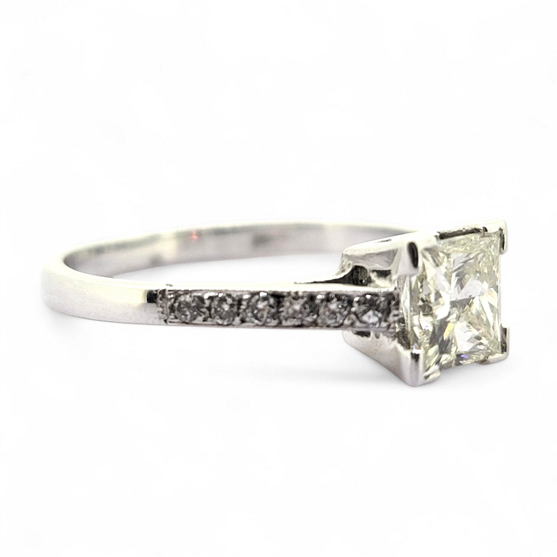 A princess cut diamond solitaire ring with diamond shoulders, in white gold, on a white background