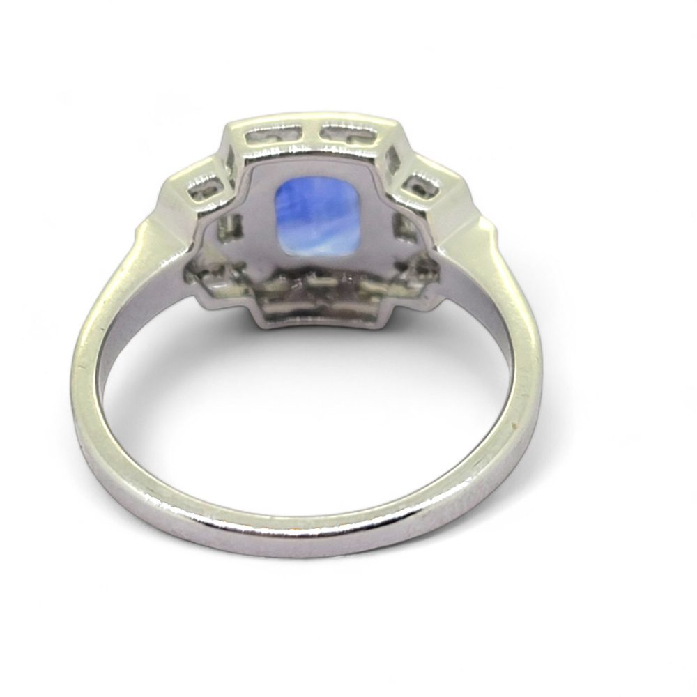 Art Deco Style 1.58ct Sapphire and Diamond Cluster Engagement Ring in 18ct White Gold, 1.58ct blue sapphire surrounded by baguette-cut diamonds with brilliant-cut diamond accents arranged in geometric design reminiscent of the Art Deco style