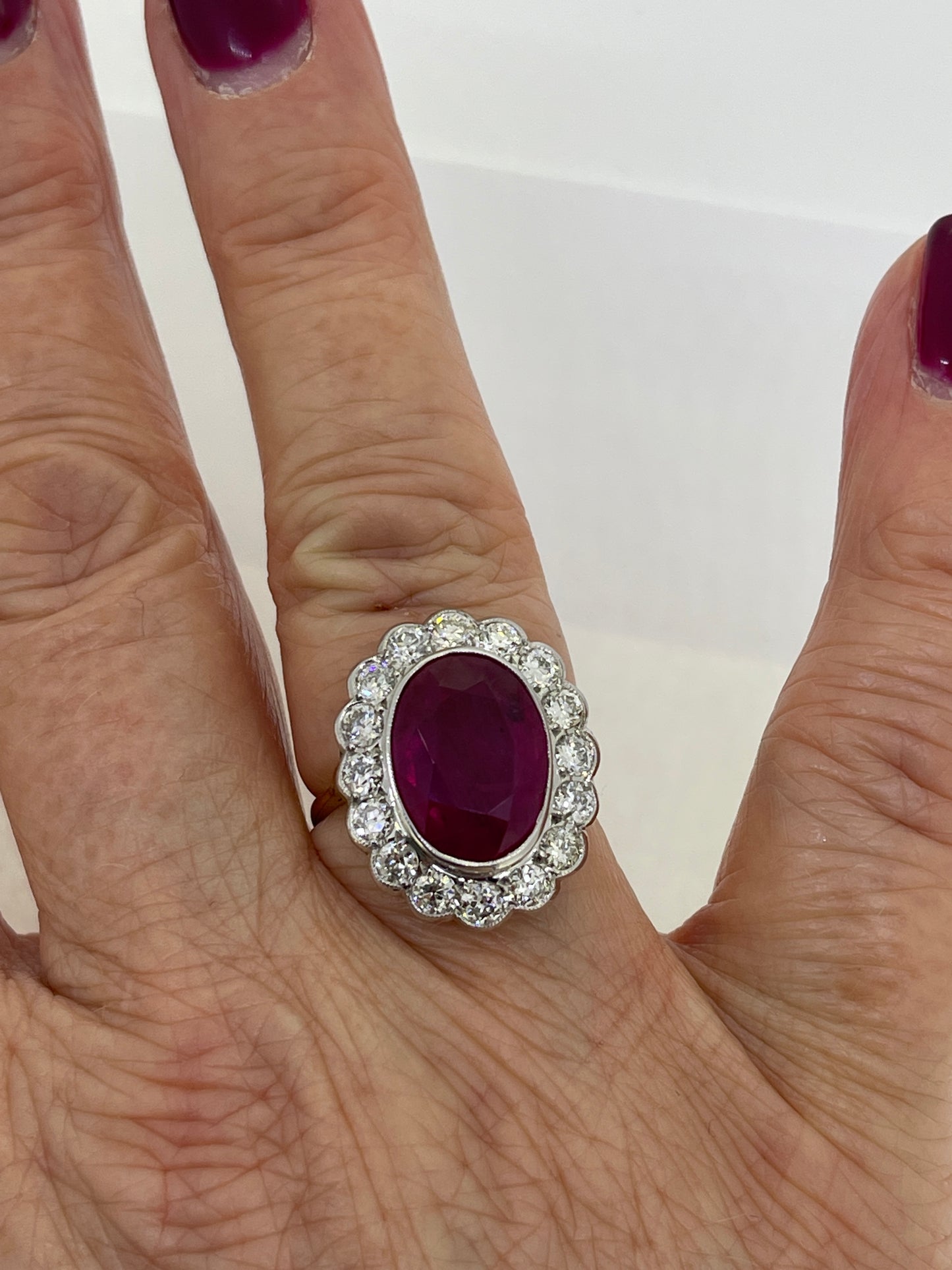 An oval ruby and round diamond scalloped edge cluster ring in yellow and white gold, modelled on a hand