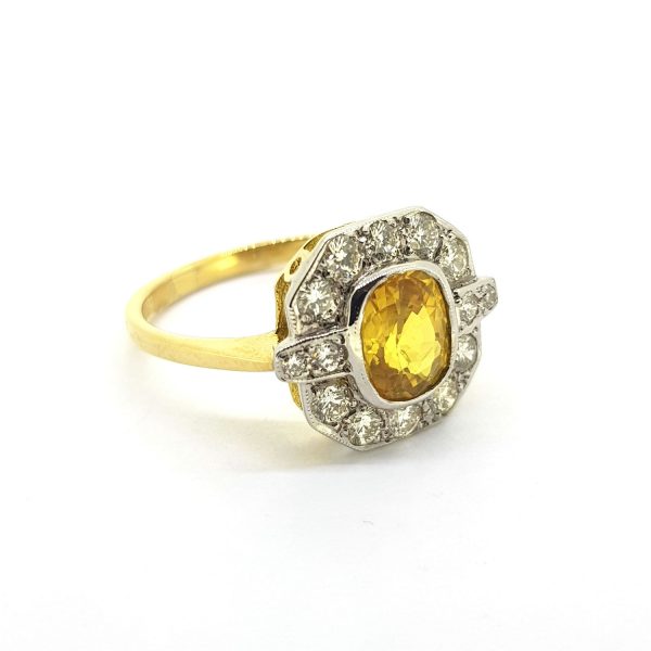 Yellow Sapphire and Diamond Cluster Ring; central 1.50ct oval yellow sapphire within a geometric diamond-set surround totalling 0.55cts, in 18ct gold