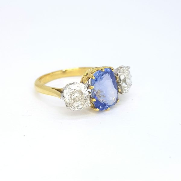 Cushion Cut Sapphire and Diamond Three Stone Ring; featuring a 3.12ct cushion-cut sapphire flanked by 2.15cts cushion-cut diamonds, in 18ct yellow gold