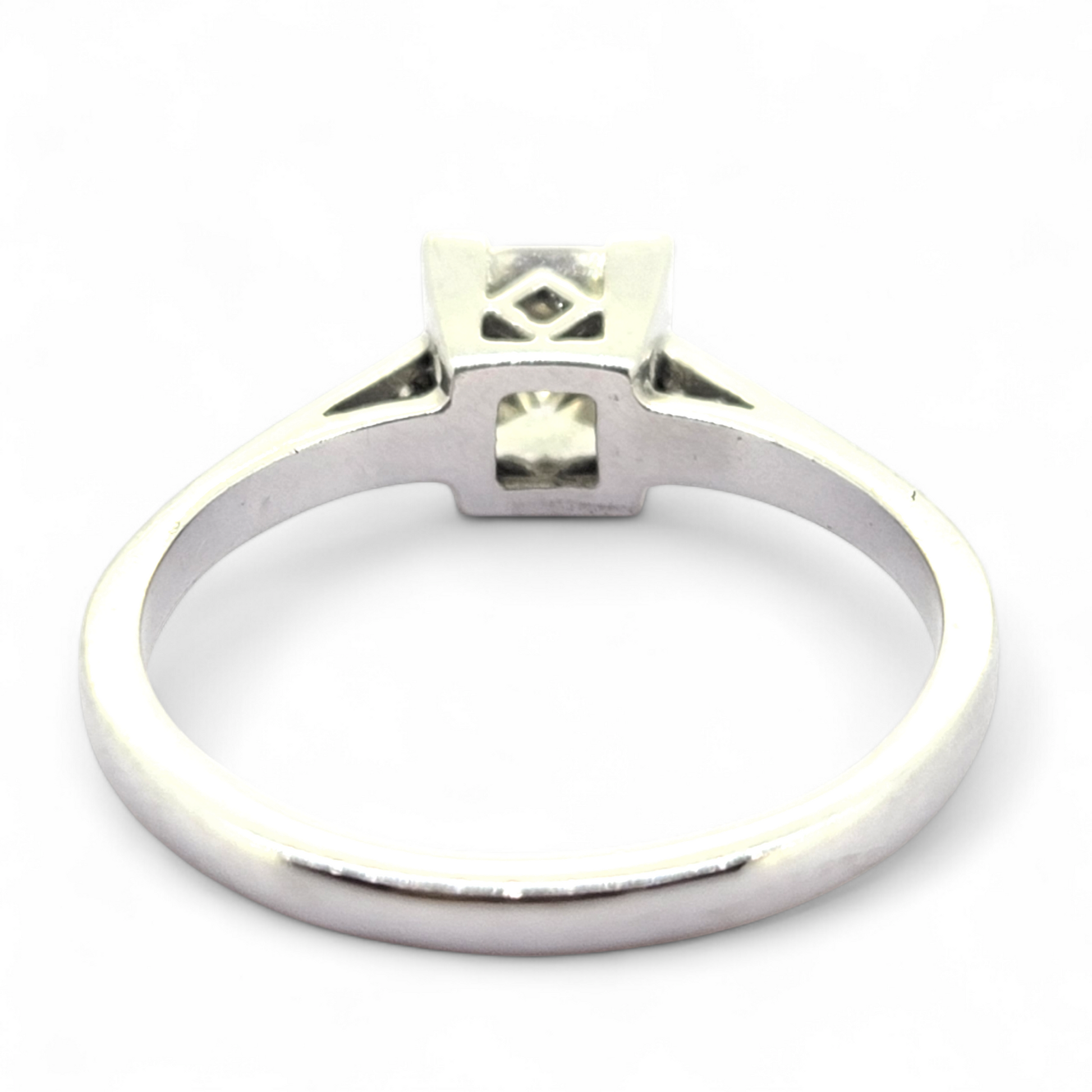 A princess cut diamond solitaire ring with diamond shoulders, in white gold, viewed from behind, on a white background