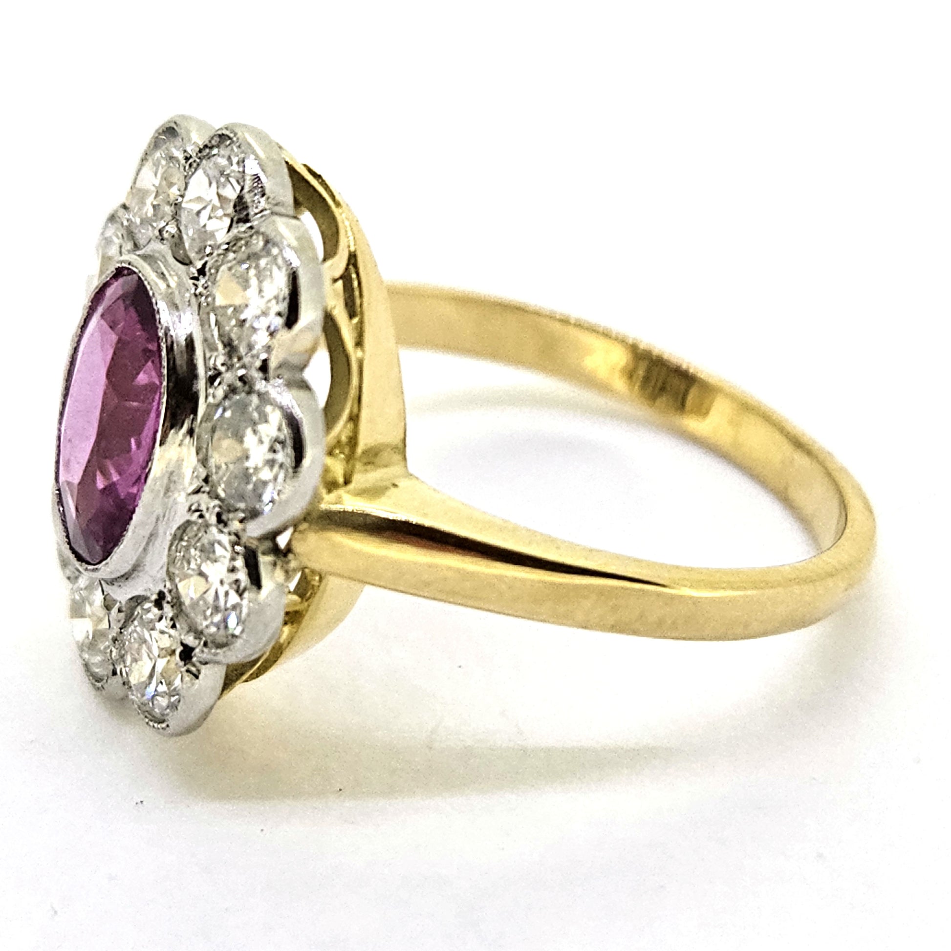 A pink sapphire and round diamond oval shaped cluster ring in yellow and white metal, on a white background