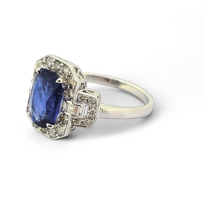 3.3ct Sapphire and Diamond Cluster Dress Ring, 3.30ct oval blue sapphire surrounded by round brilliant-cut diamonds with brilliant and baguette-cut diamond buckle style shoulders in 18ct white gold