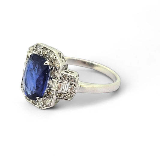 3.3ct Sapphire and Diamond Cluster Dress Ring, 3.30ct oval blue sapphire surrounded by round brilliant-cut diamonds with brilliant and baguette-cut diamond buckle style shoulders in 18ct white gold
