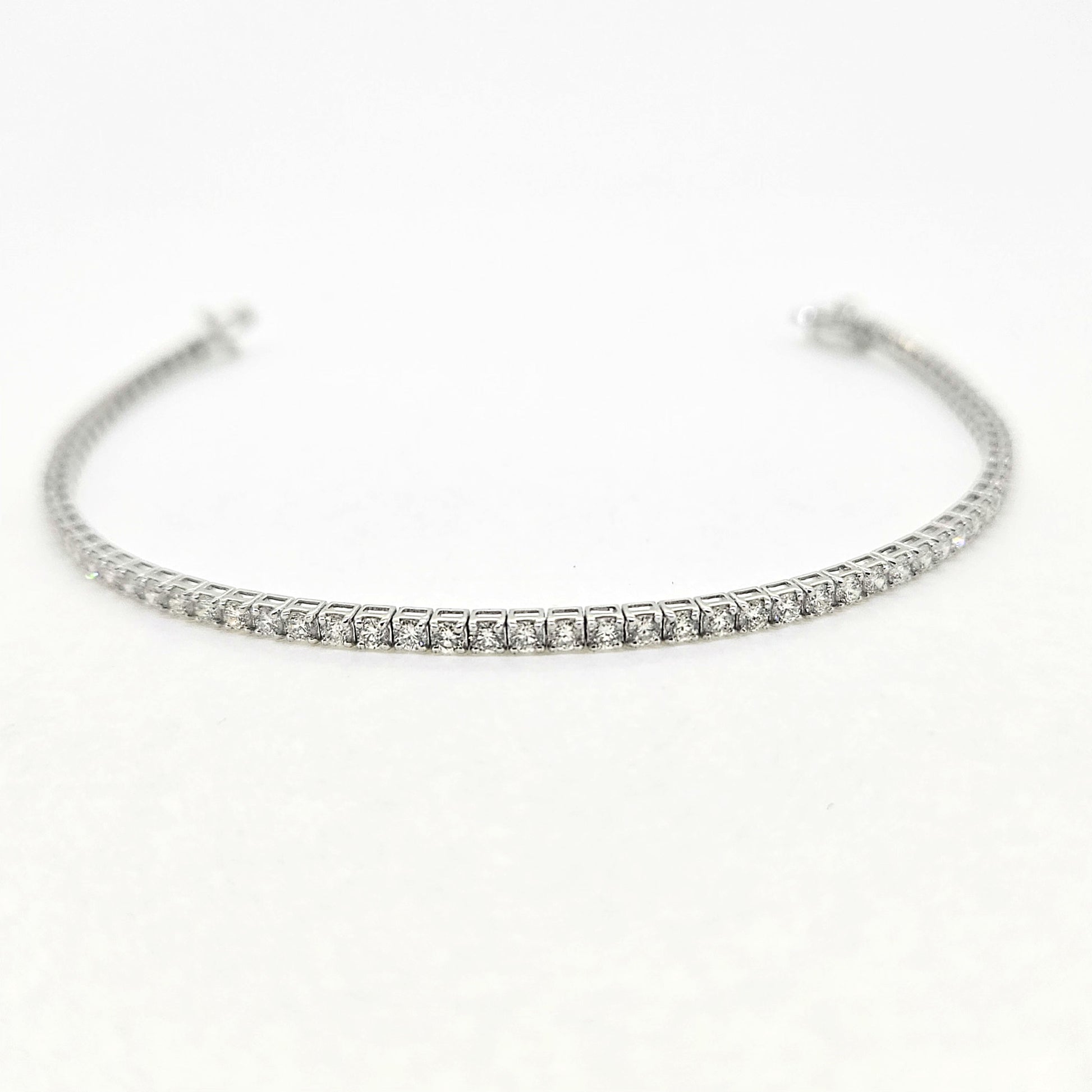 A brilliant cut diamond line bracelet, clasp open, on a white background