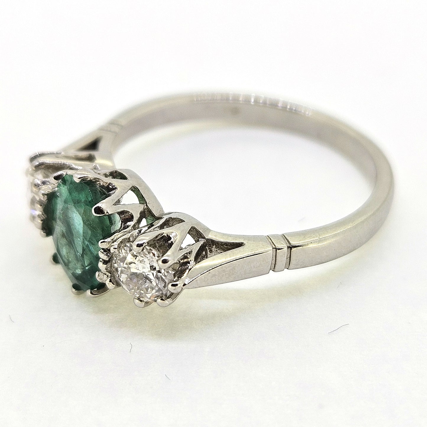 A platinum emerald and diamond three stone ring, on a white background